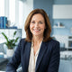A friendly middle-aged woman smiling for a professional portrait against a blurred office background with blue tones.