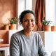 Portrait of a smiling woman in her 30s, looking confidently at the camera. The background is softly lit with terracotta and w