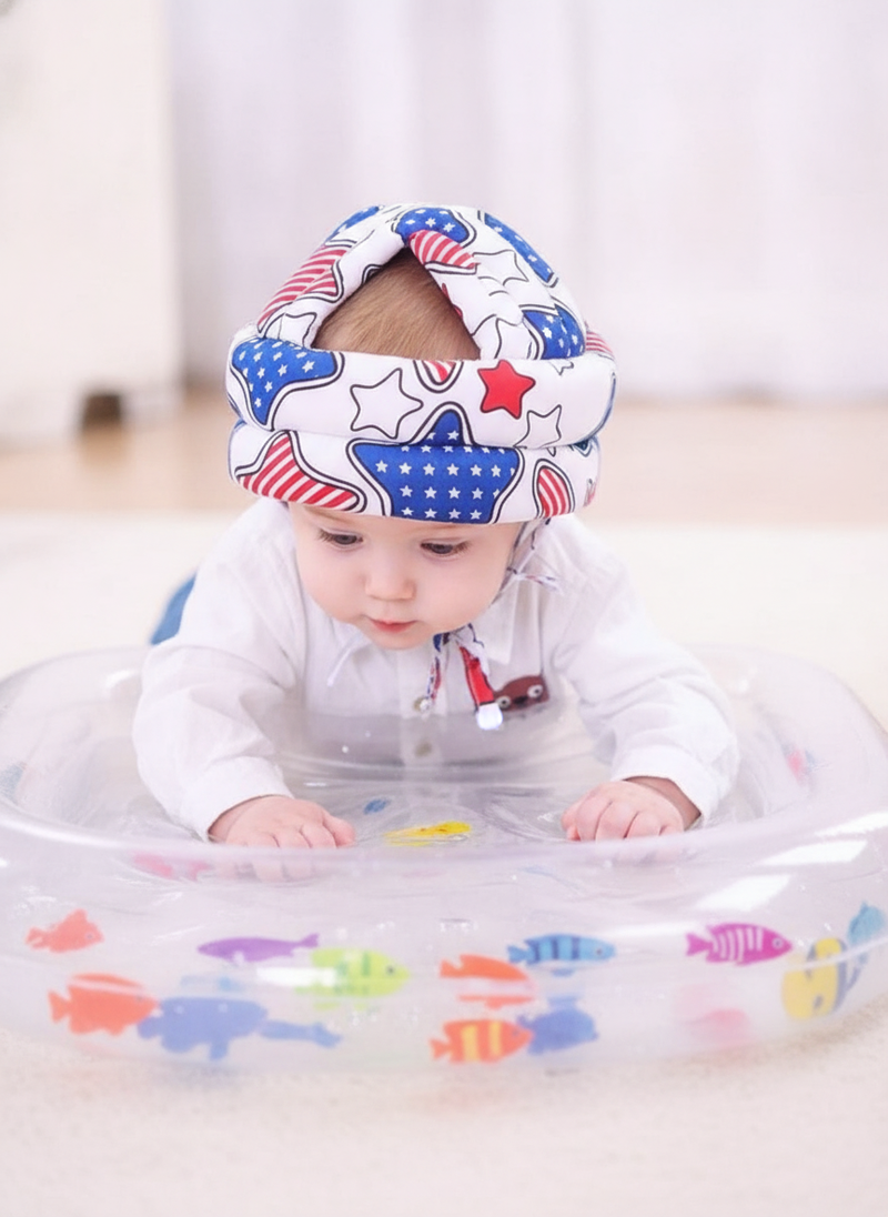 A 4-month-old baby lies on a water mat with floating fish during tummy time in a home setting. The baby looks at the fish.